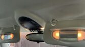 The image shows the interior roof of a MINI car with both sun visors pulled down. Each visor has a lit vanity mirror with orange lights on either side. The rearview mirror and an overhead console stand out against a beige ceiling.