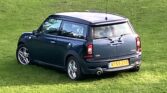 A dark blue Mini Clubman with silver trim is parked on green grass. This stylish mini car features two-part split rear doors and a yellow license plate reading "AY59 ZSE." The scene is outdoors, under daylight.