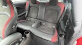 The image shows the backseat of a compact mini car with two bucket-style seats upholstered in black and red fabric. There are two headrests, seatbelt buckles, a small center divider, and cup holders on the side panels. The car appears clean and modern.