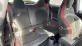 The image shows the interior of a mini car, focusing on the back seats. The seats are black leather with red accents and stitching. The two front seats are partially visible, and sunlight is shining through the rear window, illuminating the back seats.