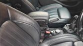 Photo of a mini car’s black leather interior, showing the front passenger and driver seats, center console with control buttons, gear shift, parking brake, and door panels. The seats have vertical stitching and the interior appears clean and well-maintained.