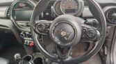 Close-up of a Mini car interior showing the steering wheel with Mini logo, dashboard with circular speedometer, control buttons, gear stick, and cup holders—all in a sleek black and silver color scheme. Perfect for any mini trader or enthusiast.