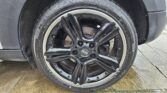 Close-up of a MINI car’s black alloy wheel and tire with the MINI logo at the center. The tire shows detailed tread and branding. Part of the car’s body is visible above, with the wheel resting on wet stone paving. Perfect for any MINI trader’s listing.