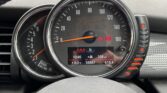 Close-up of a MINI car dashboard showing a speedometer with orange needle at zero, multiple warning lights illuminated, and a digital display reading "10:46," "8.0°C," "36667" miles, "109 mi," and "615.4." Part of the steering wheel is visible below.