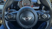 View from the driver’s seat of a Mini car, highlighting the black steering wheel with the Mini logo, dashboard controls, and central speedometer at 30 mph. A glimpse of the driver’s legs in blue jeans is visible—perfect for any mini trader or enthusiast.
