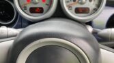Close-up of a MINI car's dashboard showing the speedometer at 0 mph, tachometer at 1300 RPM, warning lights illuminated, and an odometer reading of 64,710 miles. The black steering wheel features the classic MINI logo in the center.