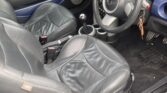 The image shows the interior of a blue Mini Cooper S, a stylish mini car. The driver and passenger seats are black leather, with round dials and blue accents on the dashboard. The steering wheel, gearstick, and car keys hanging from the ignition are also visible.