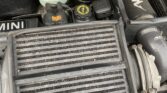 Close-up of a MINI car engine bay, highlighting an AIRTEC intercooler in the foreground. Visible details include a black “MINI” cap, white coolant reservoir, and various components—perfect for any MINI trader or enthusiast.